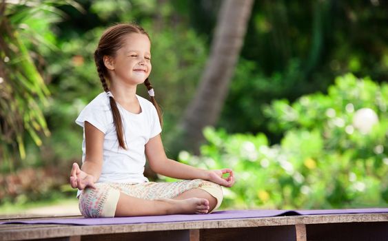 Child doing exercise on wooden platform outdoors. Healthy lifestyle. Yoga girl