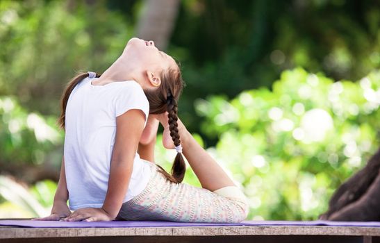 Child doing exercise on wooden platform outdoors. Healthy lifestyle. Yoga girl