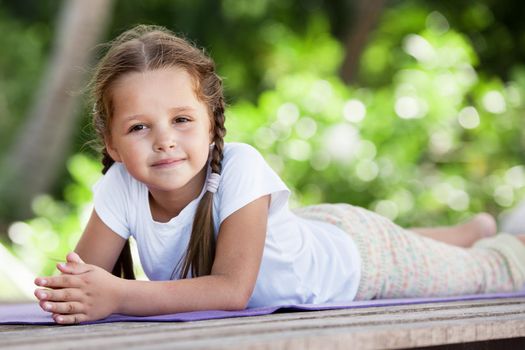 Child doing meditating exercise on wooden platform sea shore outdoors. Healthy lifestyle. Yoga girl