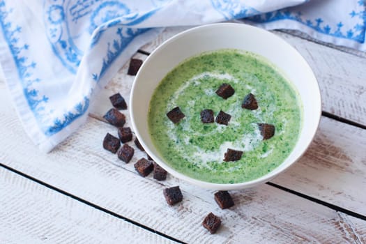 Spinach soup with croutons in red bowl on wooden table