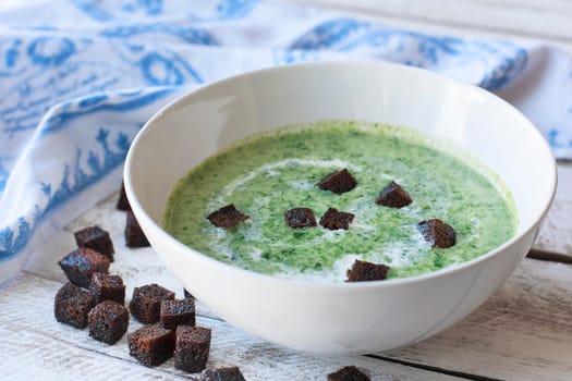 Spinach soup with croutons in red bowl on wooden table