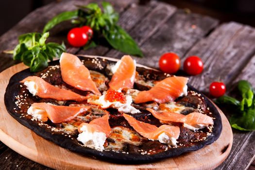 Black pizza with red fish salmon and cream cheese . Base with cuttlefish ink.