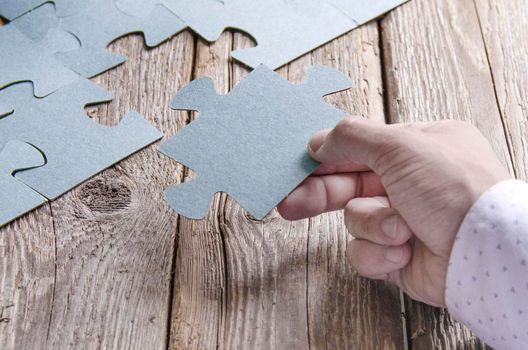 Incomplete puzzles lying on wooden rustic boards. Conceptual of innovation, solution finding and integration. Hand with puzzle piece