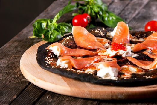 Black pizza with red fish salmon and cream cheese . Base with cuttlefish ink.