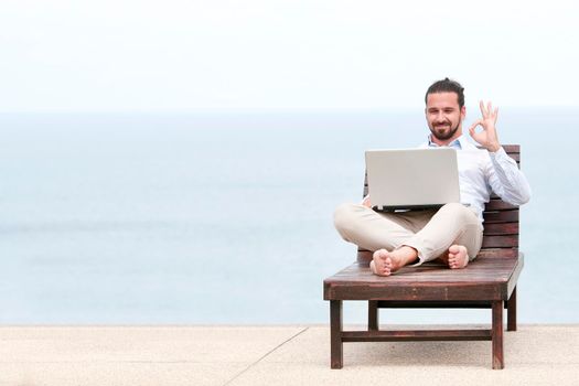 Businessman freelance on beach with laptop showing ok sign. Copy space for advertising