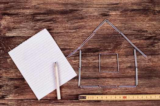 Home improvement concept - Wooden model house on a work table with tools and empty spiral notebook