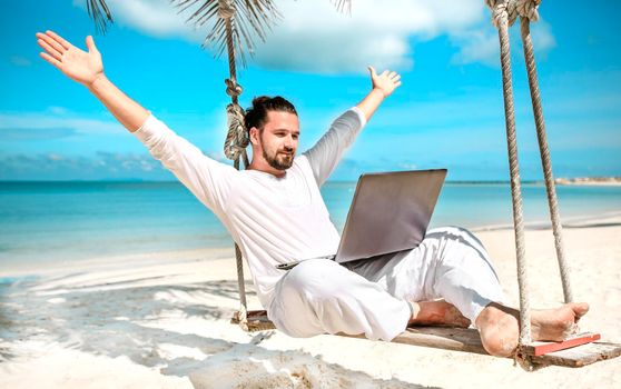 Man working with a laptop, on a hammock in the beach. Concept of digital nomad, remote worker, independent location entrepreneur. Show win