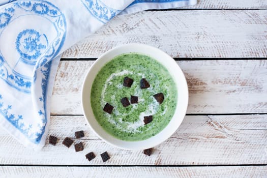 Spinach soup with croutons in red bowl on wooden table