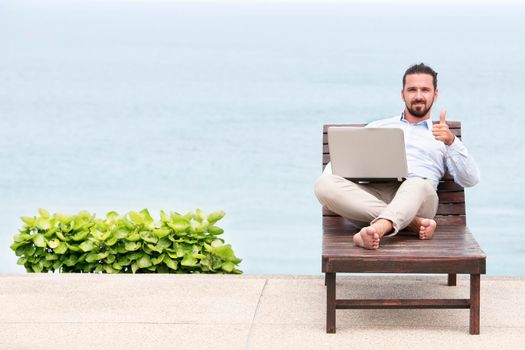 Businessman freelance on beach with laptop showing ok sign. Copy space for advertising