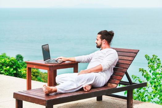 Businessman wearing white on deck chair typing laptop on the beach