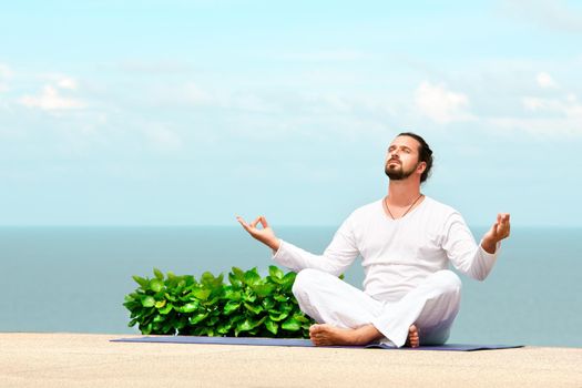 Caucasian man in white clothes meditating yoga on the sea shore pier