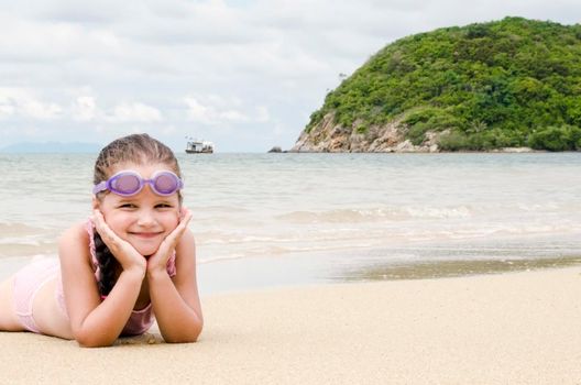 Happy little girl lying on the sand on the beach. Female preschooler kid. Copy space for text.