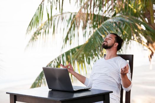 telecommuting, businessman relaxing on the beach and doing yoga with laptop and palm, freelancer workplace, dream job