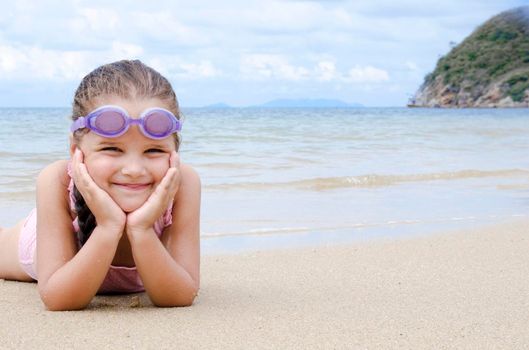 Happy little girl lying on the sand on the beach. Female preschooler kid. Copy space for text.