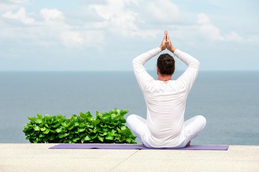 Caucasian man in white clothes meditating yoga on the sea shore pier or platform