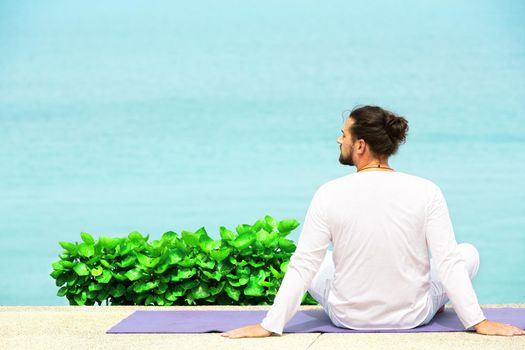 Caucasian man in white clothes meditating yoga on the sea shore pier