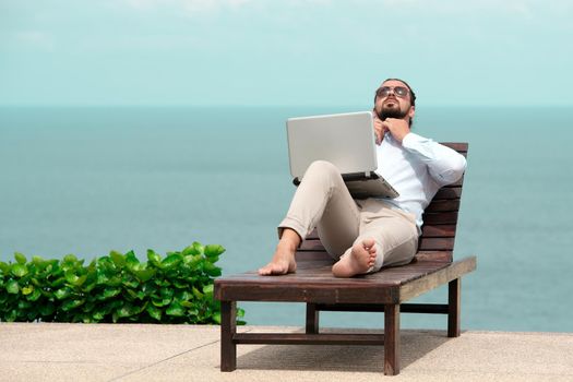 Businessman wearing a suit on deck chair typing laptop on the beach