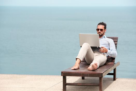 Businessman wearing a suit on deck chair typing laptop on the beach
