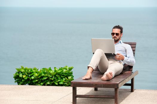 Businessman wearing a suit on deck chair typing laptop on the beach