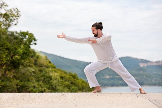Kickboxer or muay thai fighter Man in white kimono training karate or Wushu on mountain background.