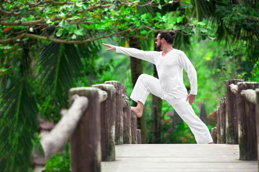 man wearingwhite doing yoga in tropic jungle bridge