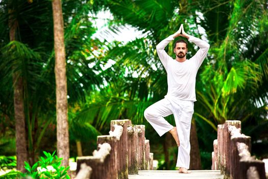 man wearing white doing yoga in tropic jungle bridge