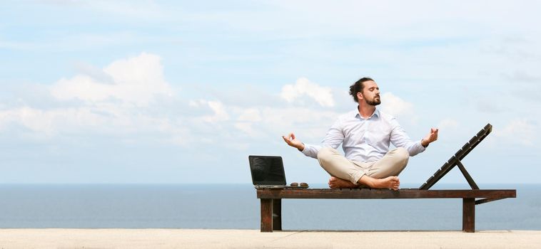 Businessman wearing a suit on deck chair doing Yoga on the beach