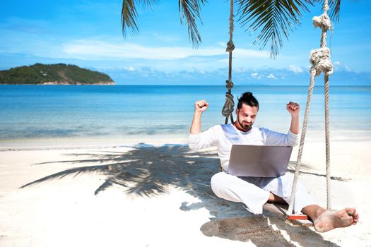 Businessman wearing white freelance sitting on beach swing with laptop