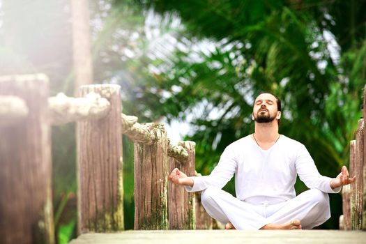 man wearing white doing yoga in tropic jungle bridge