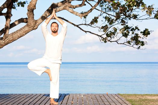 Caucasian man in white clothes meditating yoga on wooden pier