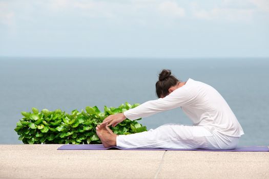Caucasian man in white clothes meditating yoga on the sea shore pier