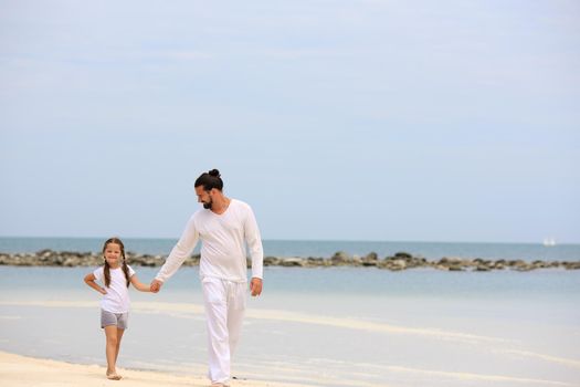 Father and daughter holding hands and walking on deserted tropical beach together happy and loving vacation