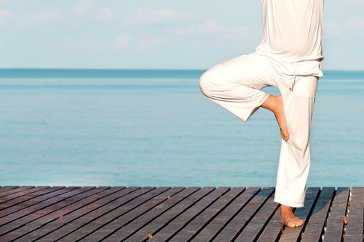 Caucasian man in white clothes meditating yoga on wooden pier