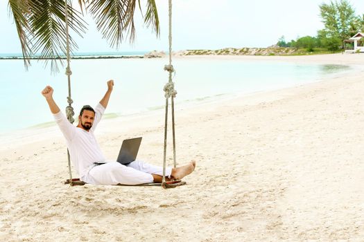 Businessman wearing white freelance sitting on beach swing with laptop