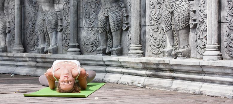 Young woman doing yoga in abandoned temple on wooden platform. Practicing in Thailand