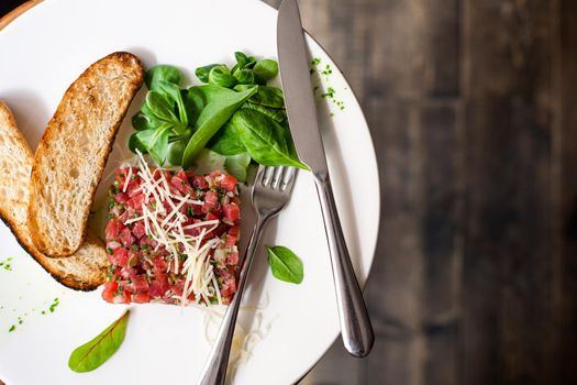 Tartare of beef with spinach on a white plate. Isolated on black or dark wooden background.