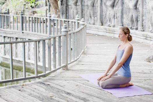 Young woman doing yoga in abandoned temple on wooden platform. Practicing in Thailand