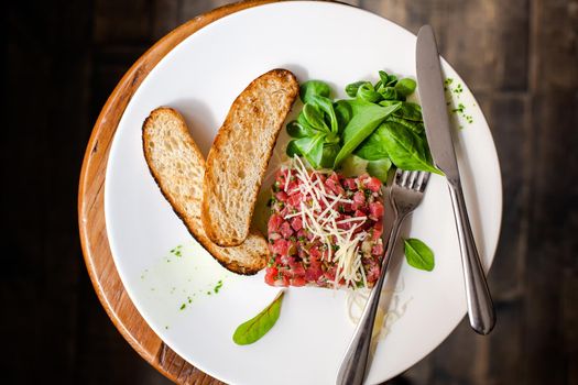 Tartare of beef with spinach on a white plate. Isolated on black or dark wooden background.