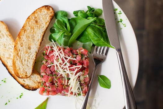 Tartare of beef with spinach on a white plate. Isolated on black or dark wooden background.