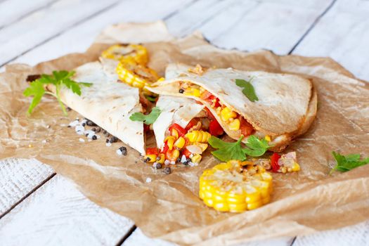 Mexican Quesadilla wrap with vegetables, corn, sweet pepper and sauces on the parchment and table. horizontal view.