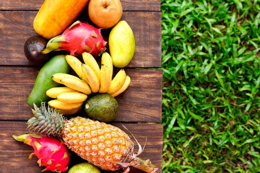 Fresh fruits. Mixed exotic fruits on wood background. Healthy eating, dieting. Top view with grass copy space