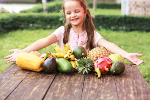 Exotic fruit on wooden table. Summer background with small Laughing happy girl