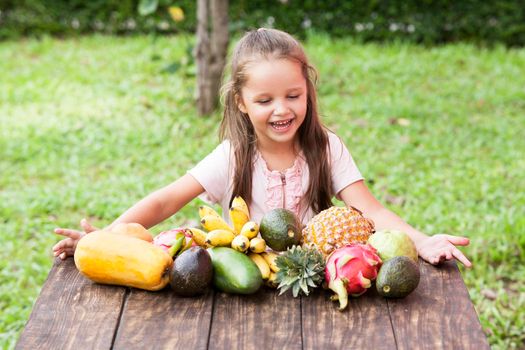 Exotic fruit on wooden table. Summer background with small Laughing happy girl