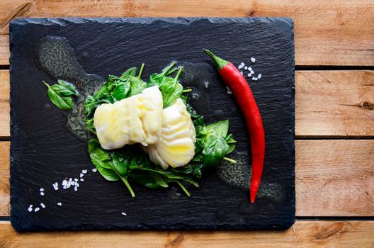 White fish fillet with herbs and chili on fried spinach. Gray background.