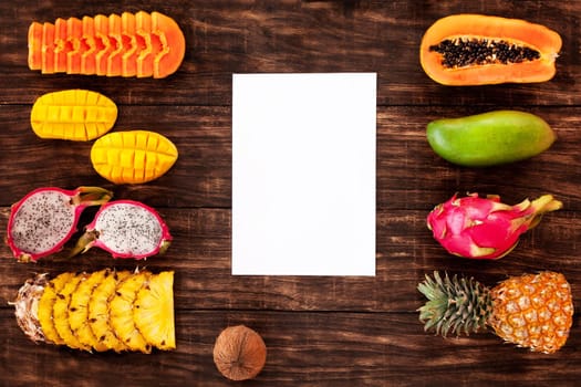 Fresh Tropical fruit on dark wooden background, top view, with white board in center, copy space