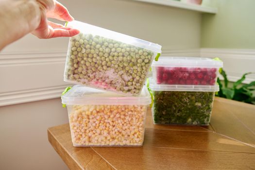 Frozen vegetables and fruits, close-up frozen in the freezer green onions, peas, cherry, corn in plastic containers. Seasonal vegetables, food preparations for the winter