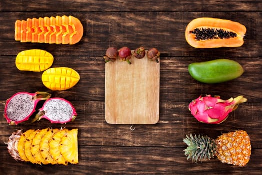 Fresh Tropical fruit on dark wooden background, top view, with white board in center, copy space