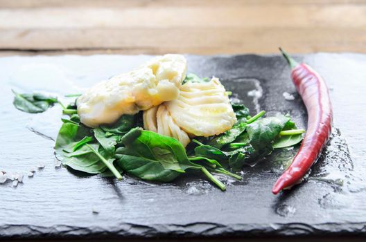 White fish fillet with herbs and chili on fried spinach. Gray background.