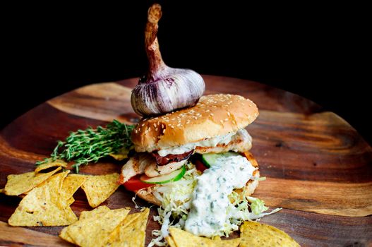 Creatively styled beef burger with rustic home-made French chips or crisps shot against a dark background with generous accommodation for copy space. garlic on top
