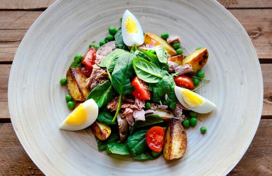 Tuna salad with lettuce, eggs and tomatoes on wooden plate